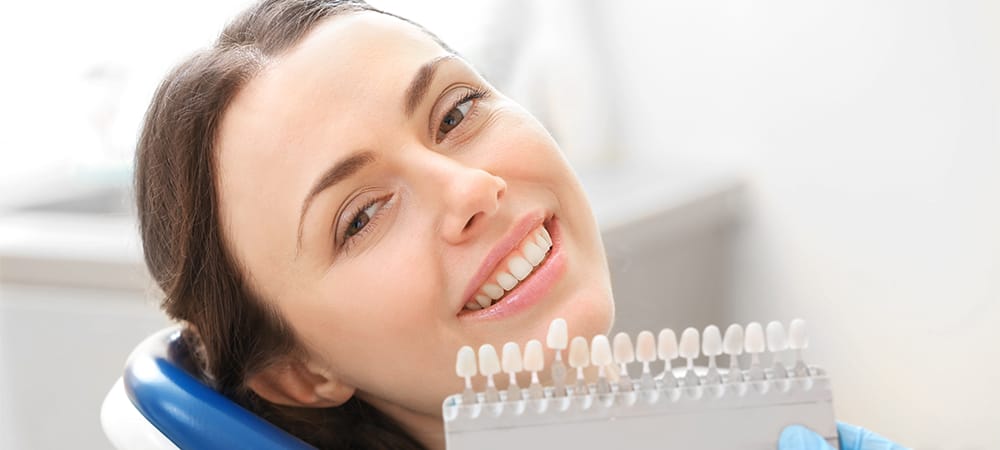 dentist checking and selecting color of young woman teeth