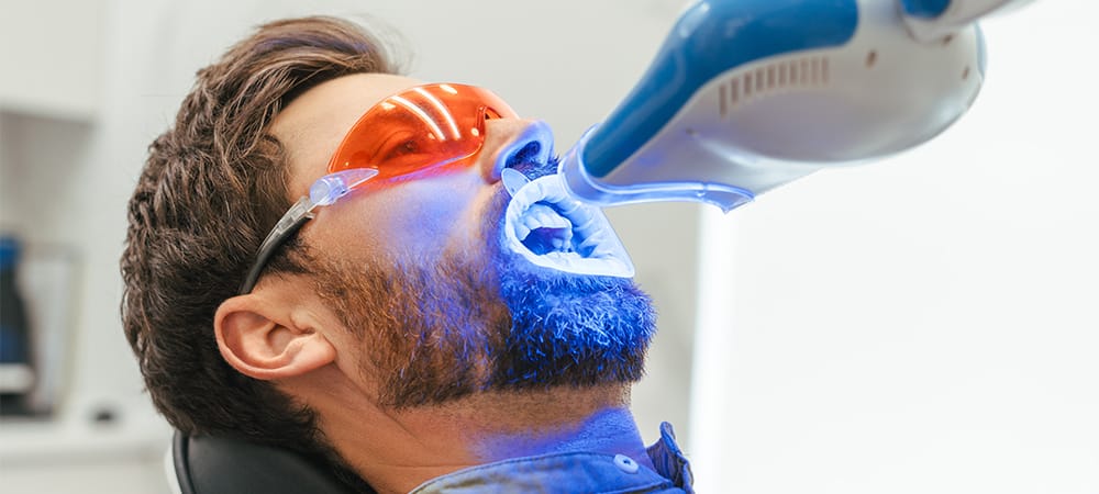 man patient whitening teeth in modern dental clinic, laser whitening or light-activated treatments