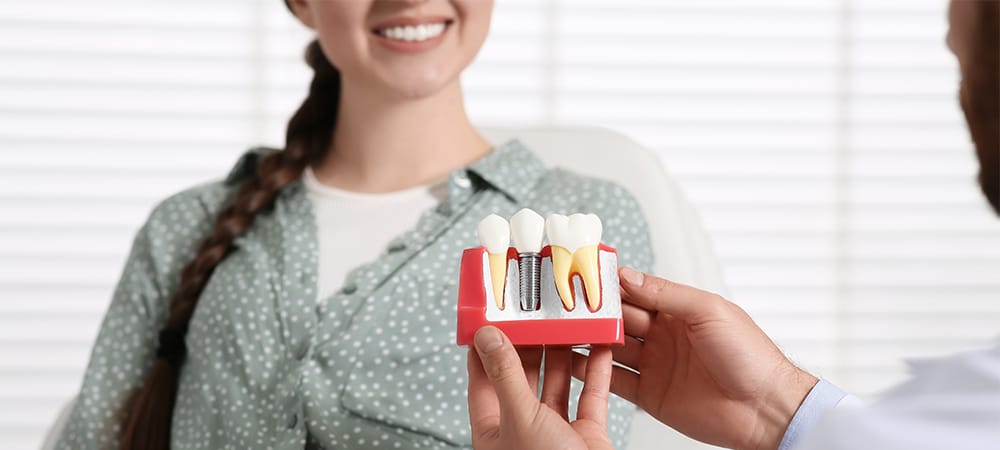 doctor with educational model of dental implant consulting patient in clinic, closeup