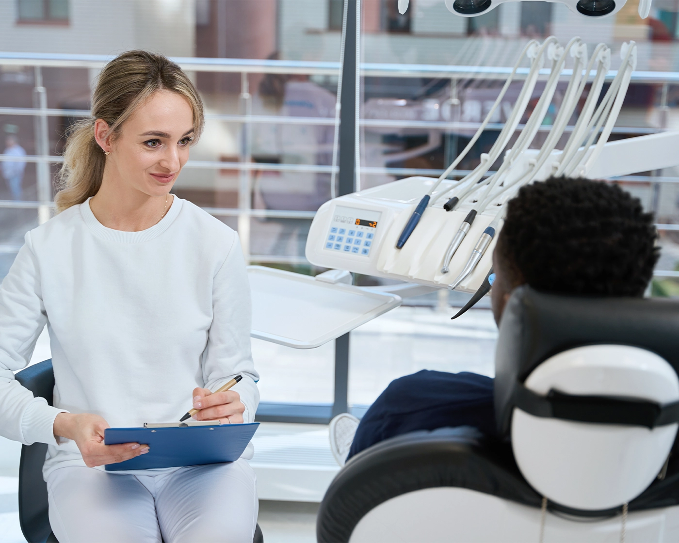Attentive young doctor stomatologist attentively listening to African American man lying in dental chair and complaining on sharp toothache