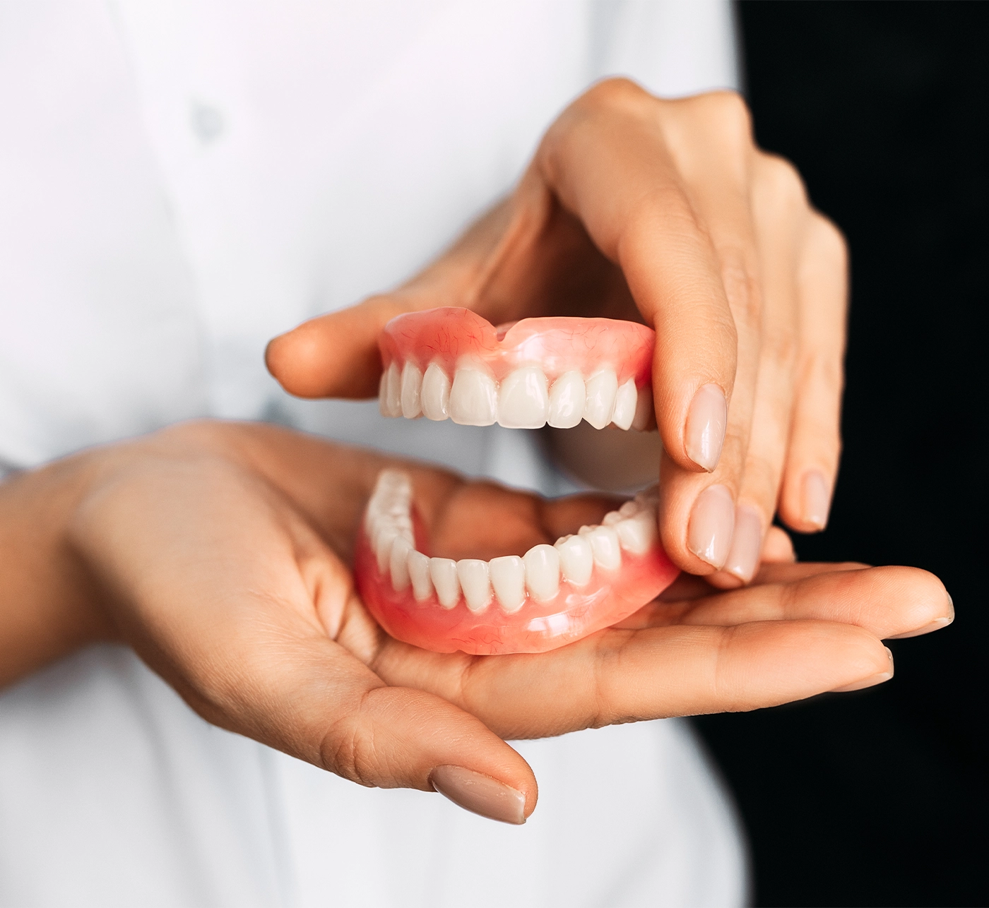 The dentist is holding dentures in his hands. Dental prosthesis in the hands of the doctor close-up. Front view of complete denture