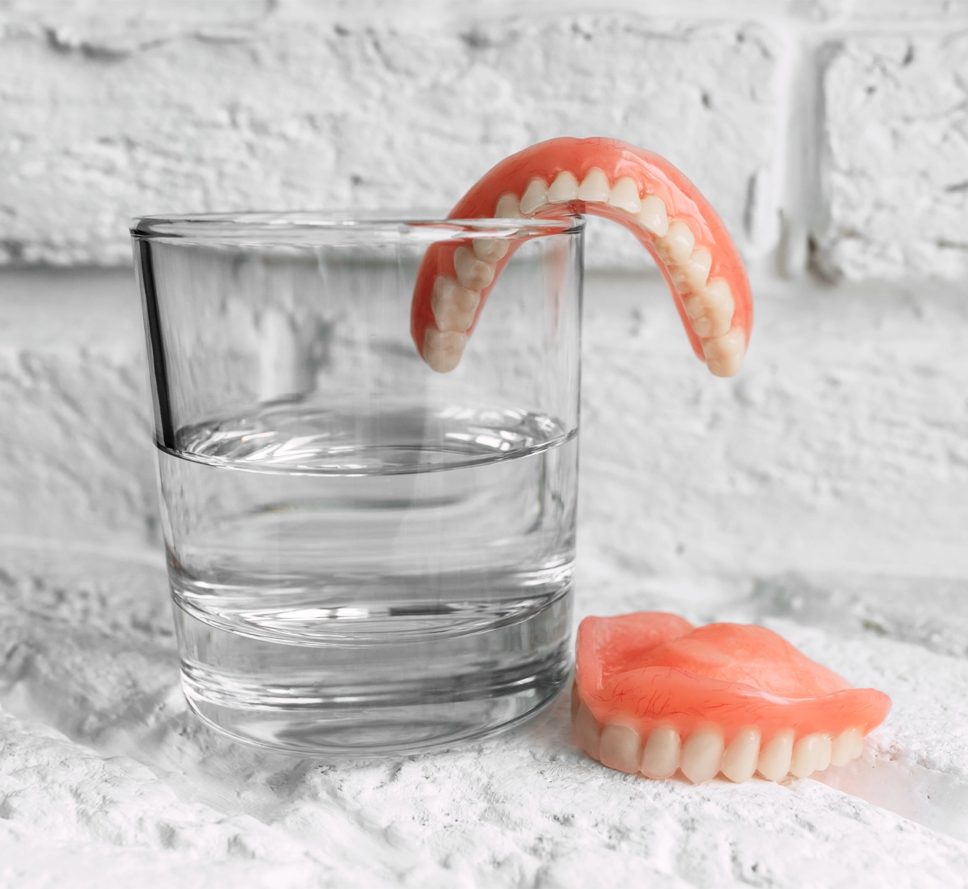 A denture in a glass of water. Dental prosthesis care. Full removable plastic denture of the jaws. Two acrylic dentures. Upper and lower jaws with fake teeth. Dentures or false teeth, close-up.