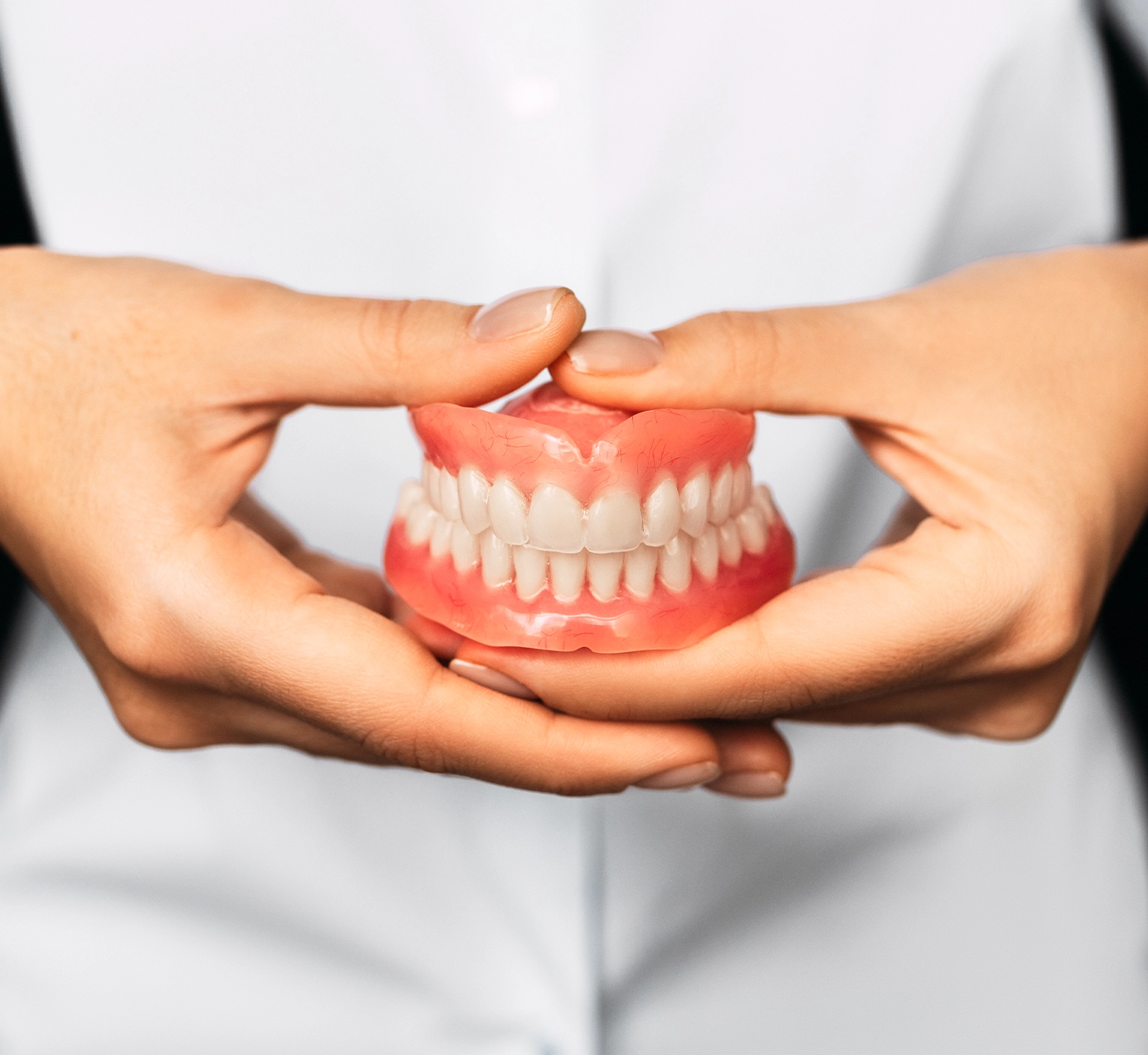 The dentist is holding dentures in his hands. Dental prosthesis in the hands of the doctor close-up. Front view of complete denture