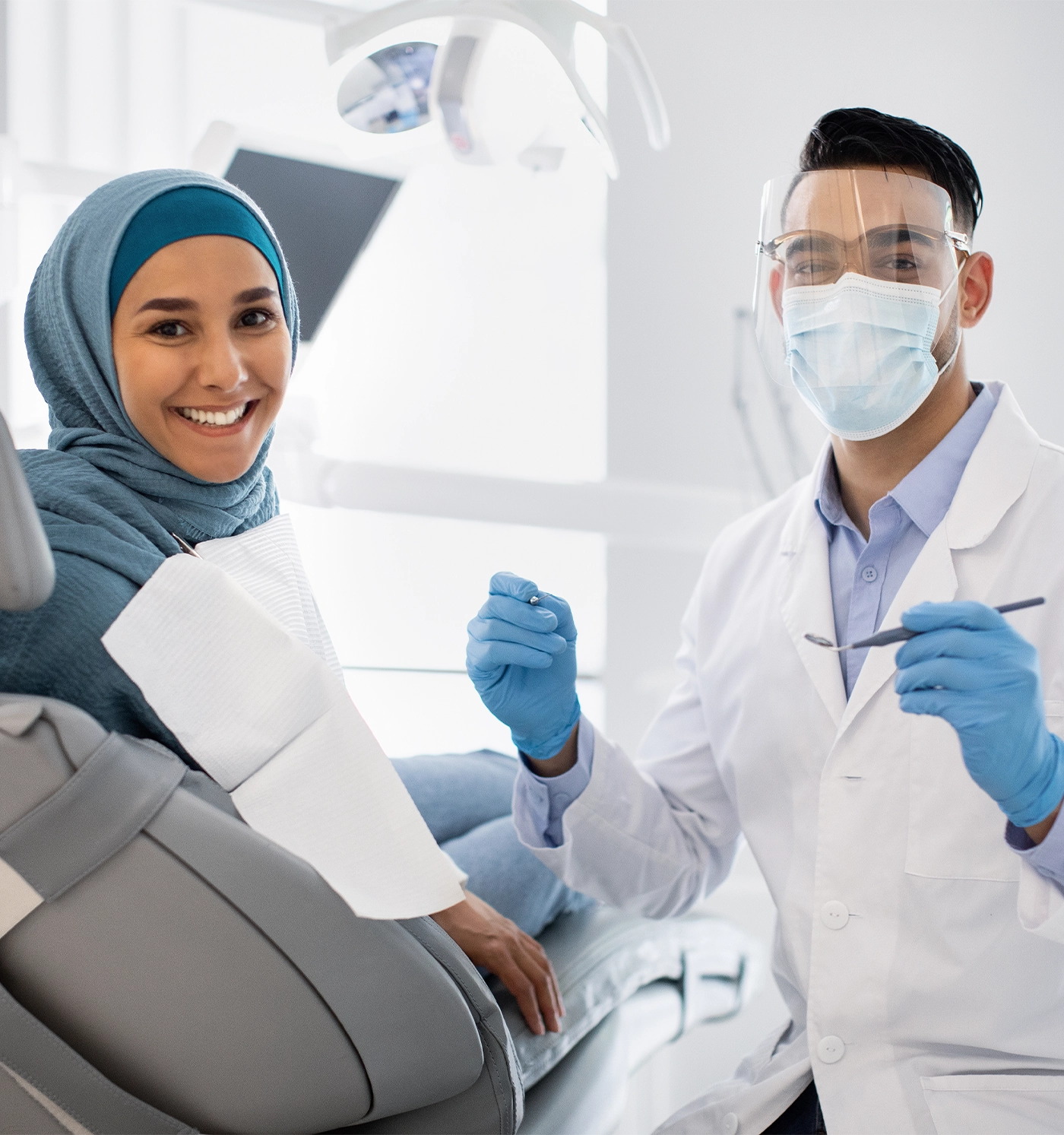 Root Canal Treatment. Stomatologist Man In Medical Mask And Face Shield Having Checkup With Muslim Female Patient In Hijab, Middle Eastern Doctor Holding Dental Tools And Looking At Camera