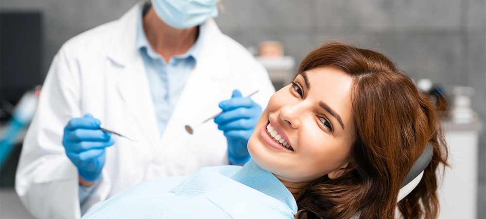 Portrait of a young European woman smiling, looking at the camera, with a dentist in the background and a dental office setting.
